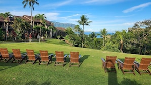 Une pelouse d’un complexe hôtelier, avec des rangées de chaises et une vue sur une montagne et l’océan.