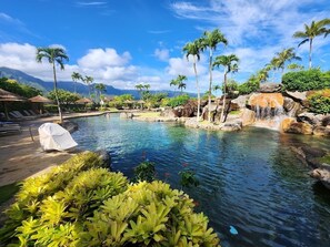 Un espace piscine agrémenté de chaises longues, de palmiers et d’une cascade.