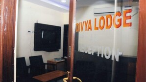 Ett receptionsområde med en glasdörr, en tv som är monterad på väggen och en skylt med texten ”Divya Lodge Reception”.