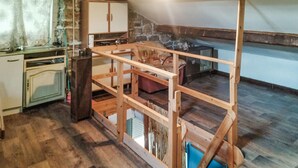 Une pièce dotée d’une structure de lit en hauteur en bois, d’un mur en pierre et d’un coin cuisine avec des placards et un évier.