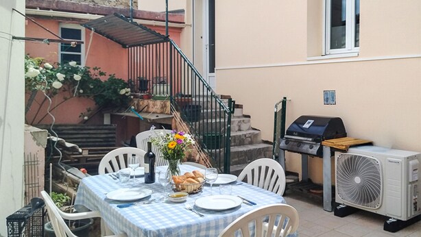 Un espace extérieur aménagé pour les repas, avec une table pour deux personnes, un barbecue et un ventilateur.
