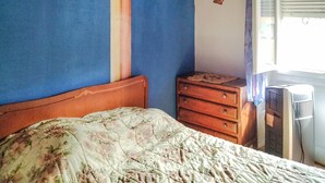 Une chambre à coucher comprenant un lit, une commode, une horloge murale et une fenêtre avec des stores.