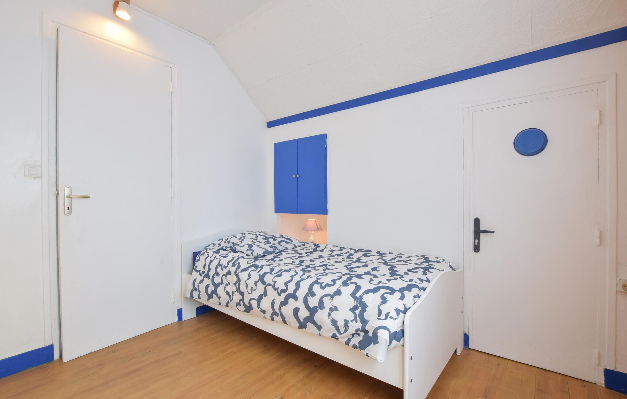 A small, single-bed room with a curved ceiling, white walls, and a wooden floor.