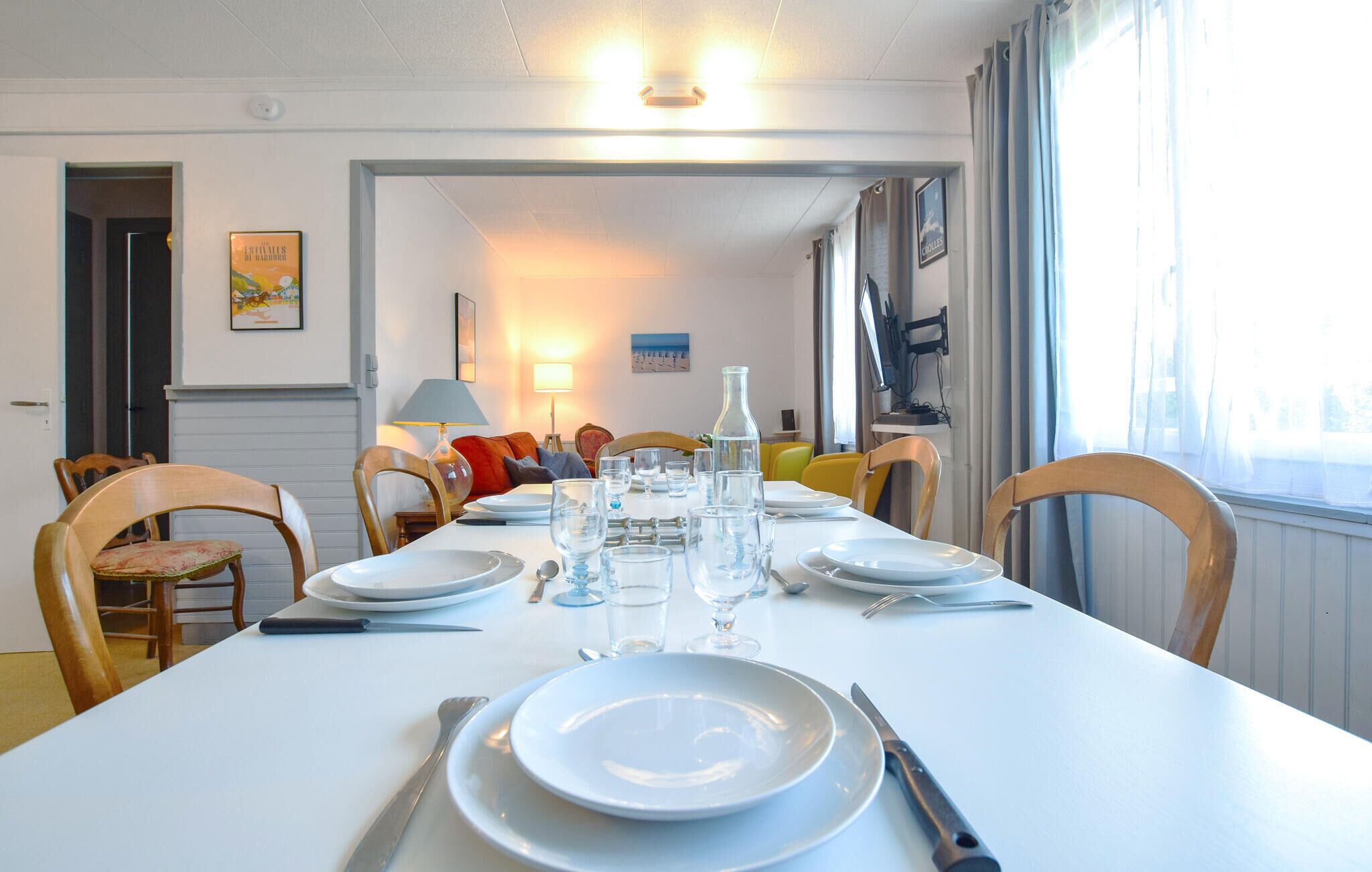Une salle à manger avec une table blanche dressée pour quatre personnes, des chaises et une lampe.
