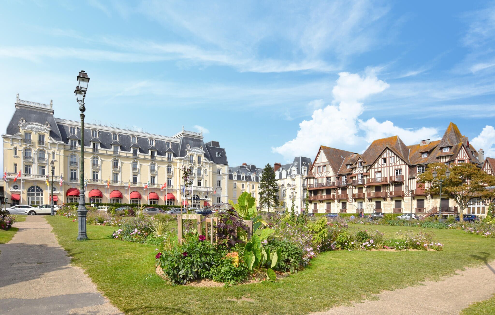 Ein historisches Gebäude mit einer großen Fassade, einem Garten mit verschiedenen Pflanzen und einem strahlend blauen Himmel.