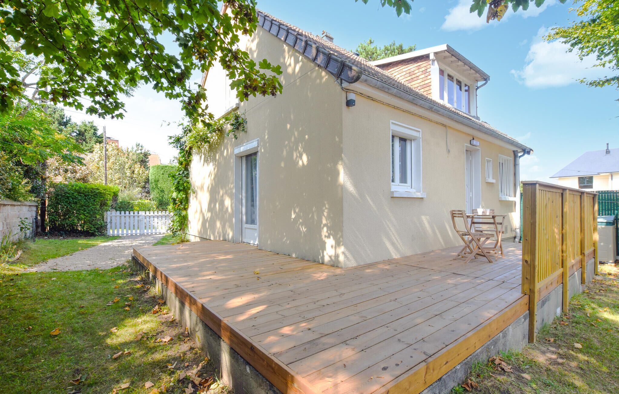 Une maison à deux étages dotée d’une terrasse en bois et d’un petit espace patio.