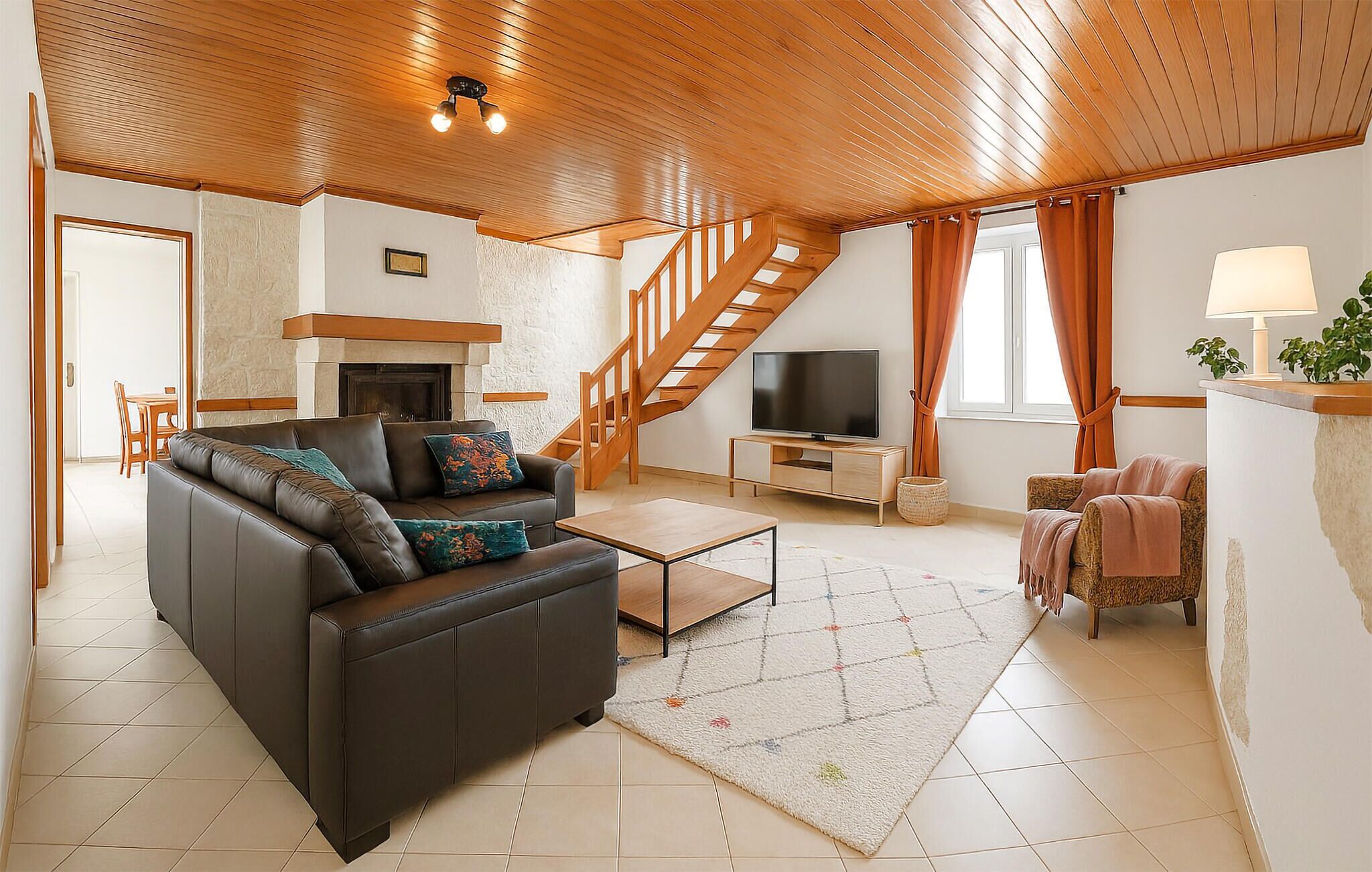 A spacious living room with a leather sofa, a coffee table, a TV, and a staircase leading to an upper level.