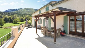 A covered outdoor patio with a table and chairs, a small garden area, and a view of a mountainous landscape.