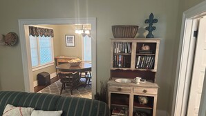 Un salon chaleureux avec un canapé à rayures vertes, une table d’appoint en bois sur laquelle se trouvent un bol et des livres, et un coin repas avec une table et des chaises.