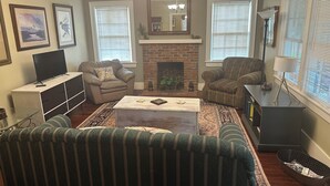 Un salon avec une cheminée, deux fauteuils, un canapé, une table basse et un téléviseur.