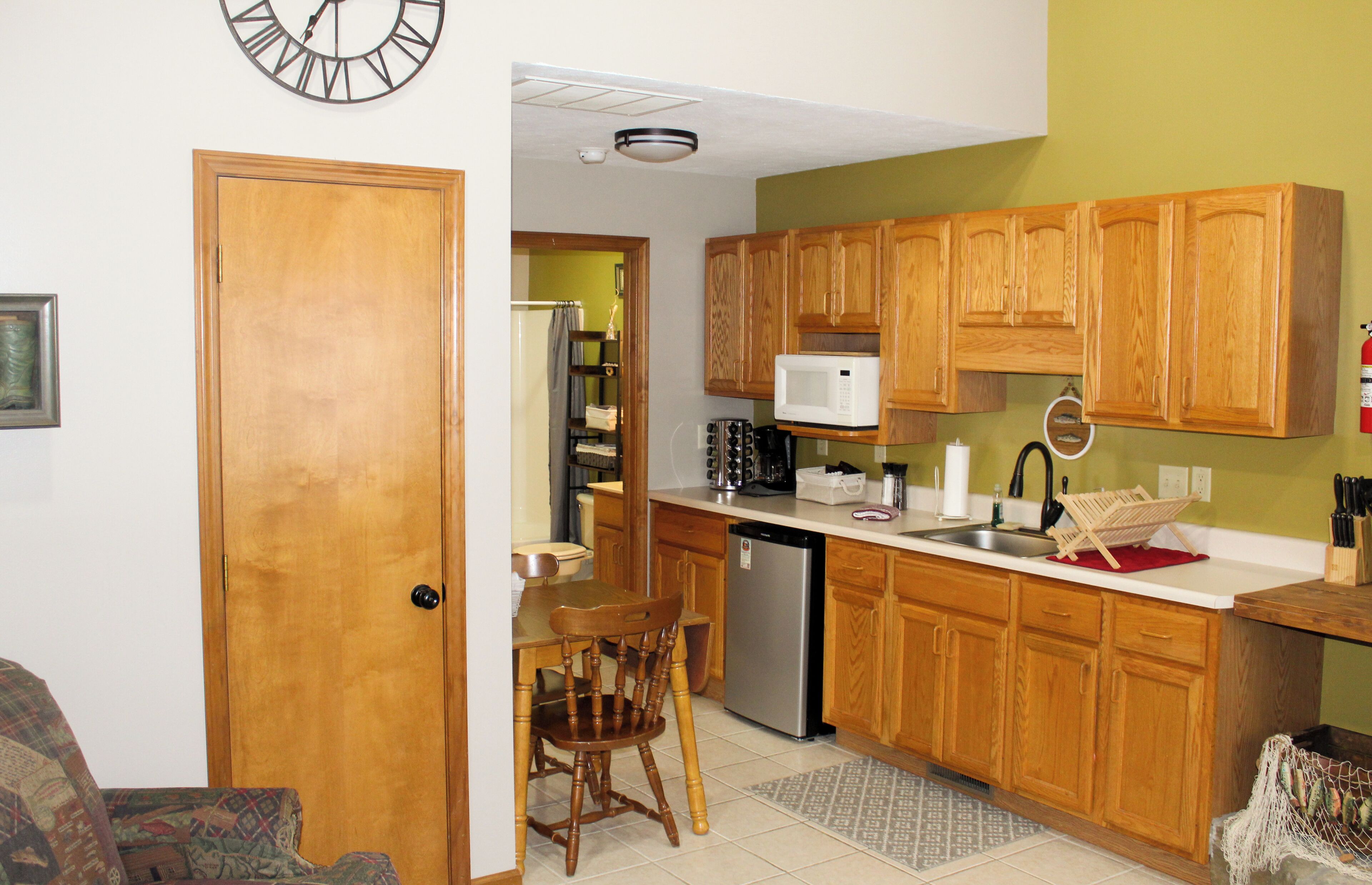 A compact kitchen with wooden cabinets, a microwave, a dishwasher, and a dining area with a chair and table.