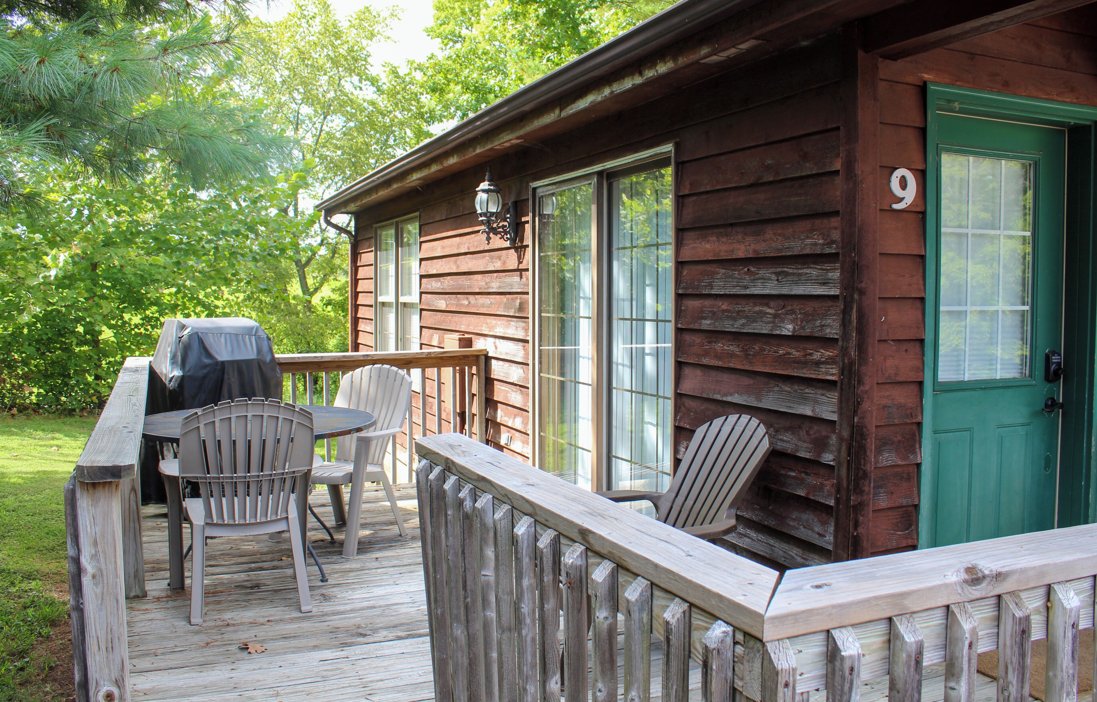 A wooden cabin with a deck, a barbecue grill, and two chairs.