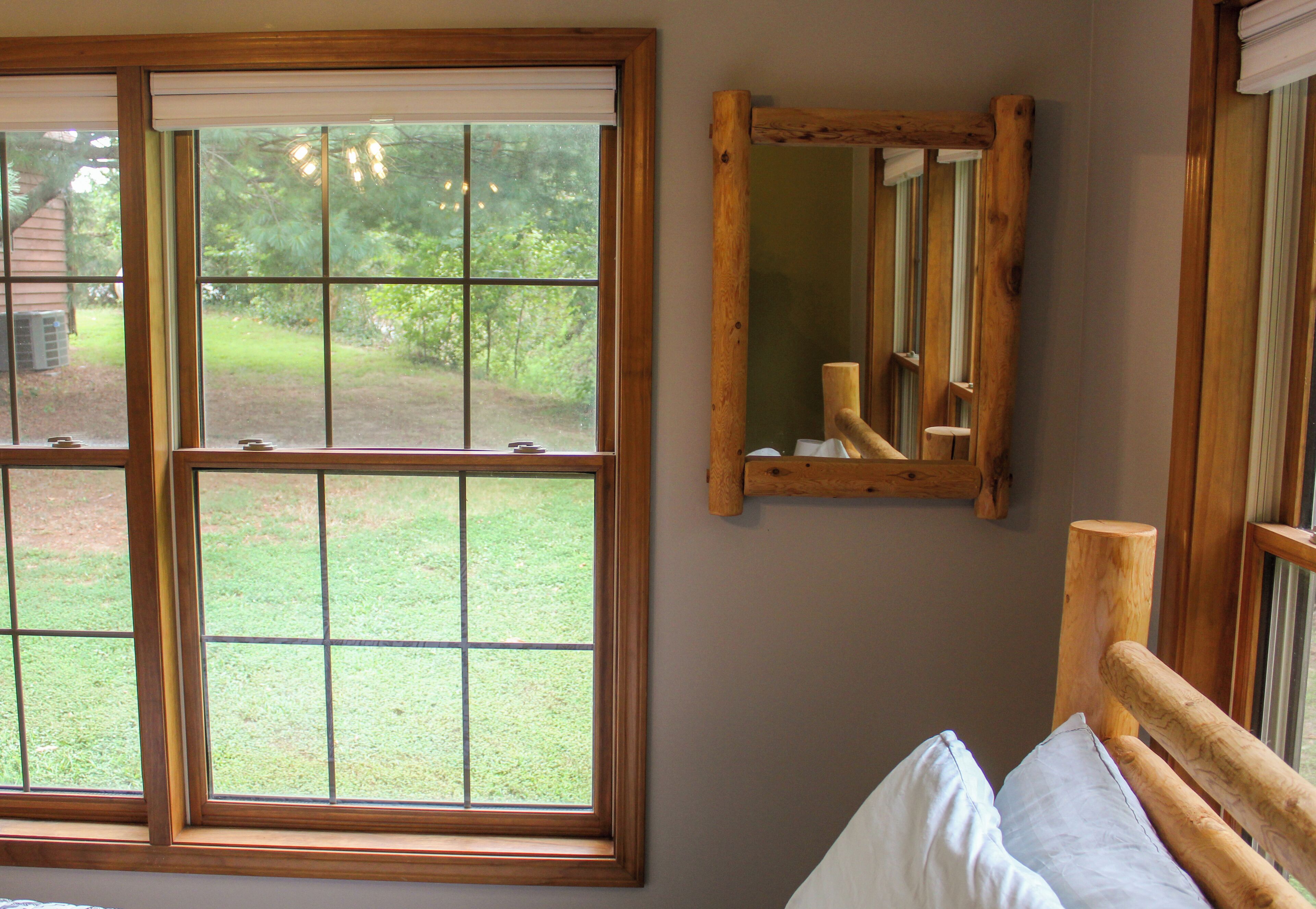A room with a large window, a wooden headboard, and a mirror on the wall.