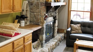 A kitchen with wooden cabinets, a stone fireplace, a flat-screen TV above it, and a dining area with a wooden table and chairs. - Minutes from Giant City - SIU - Shawnee Winetrail - Shawnee Forest - Cedar Lake (Makanda)