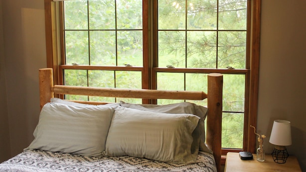 A bed with a wooden headboard, a window with a view of greenery, and a bedside table with a lamp and a remote control. - Minutes from Giant City - SIU - Shawnee Winetrail - Shawnee Forest - Cedar Lake (Makanda)