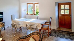 A dining area with a table set for four, surrounded by wicker chairs, a wooden chair, and a television on the left.