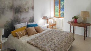 A bedroom with a bed, a window, a chair, a table, and a lamp.