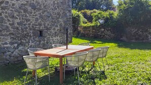 A stone building with a wooden table and six chairs in a garden setting.