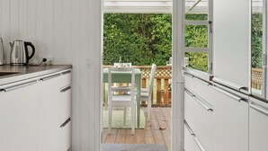 A narrow kitchen with white cabinetry and a view to an outdoor deck. - Renovated classic cottage close to beach (Roslev)