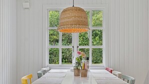 A dining area with a white table, yellow and green chairs, a hanging basket light, and a window with greenery outside. - Renovated classic cottage close to beach (Roslev)