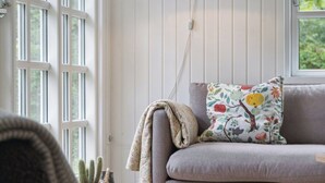 A room with a sofa, a lamp, a window, and a cactus. - Renovated classic cottage close to beach (Roslev)