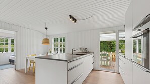 A modern kitchen with white cabinetry, a central island, and a dining area with a table and chairs. - Renovated classic cottage close to beach (Roslev)