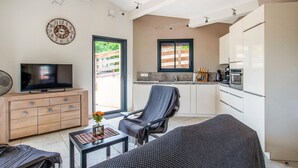 A compact living space with a TV, sofa, dining table, and kitchenette.