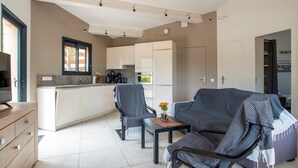 A modern kitchen with white cabinets, a dining area with two chairs, and a sofa.