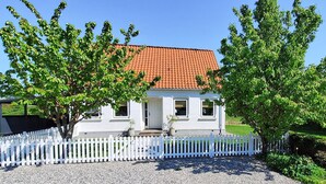 A white house with a red-tiled roof, surrounded by a white picket fence, and trees in front. - Beautiful home in ærøskøbing with WiFi (Ærøskøbing)