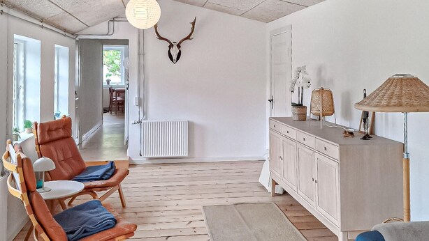 A spacious living room with a high ceiling, a wooden floor, a dining area in the background, and a large cabinet with drawers. - Beautiful home in ærøskøbing with WiFi (Ærøskøbing)