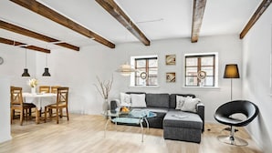 A modern living room with a grey sectional sofa, a glass coffee table, wooden dining table with chairs, and exposed wooden beams on the ceiling. - Beautiful apartment in Tommerup (Tommerup)
