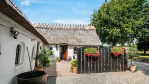 A rustic building with a thatched roof, a wooden fence with hanging flower baskets, and potted plants. - Beautiful apartment in Tommerup (Tommerup)