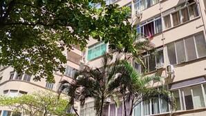 Un edificio de varios pisos con balcones, unidades de aire acondicionado y un árbol en primer plano.
