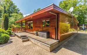 Une cabane moderne en bois, dotée d’un porche couvert, d’une antenne parabolique et d’un chemin en briques menant à l’entrée.