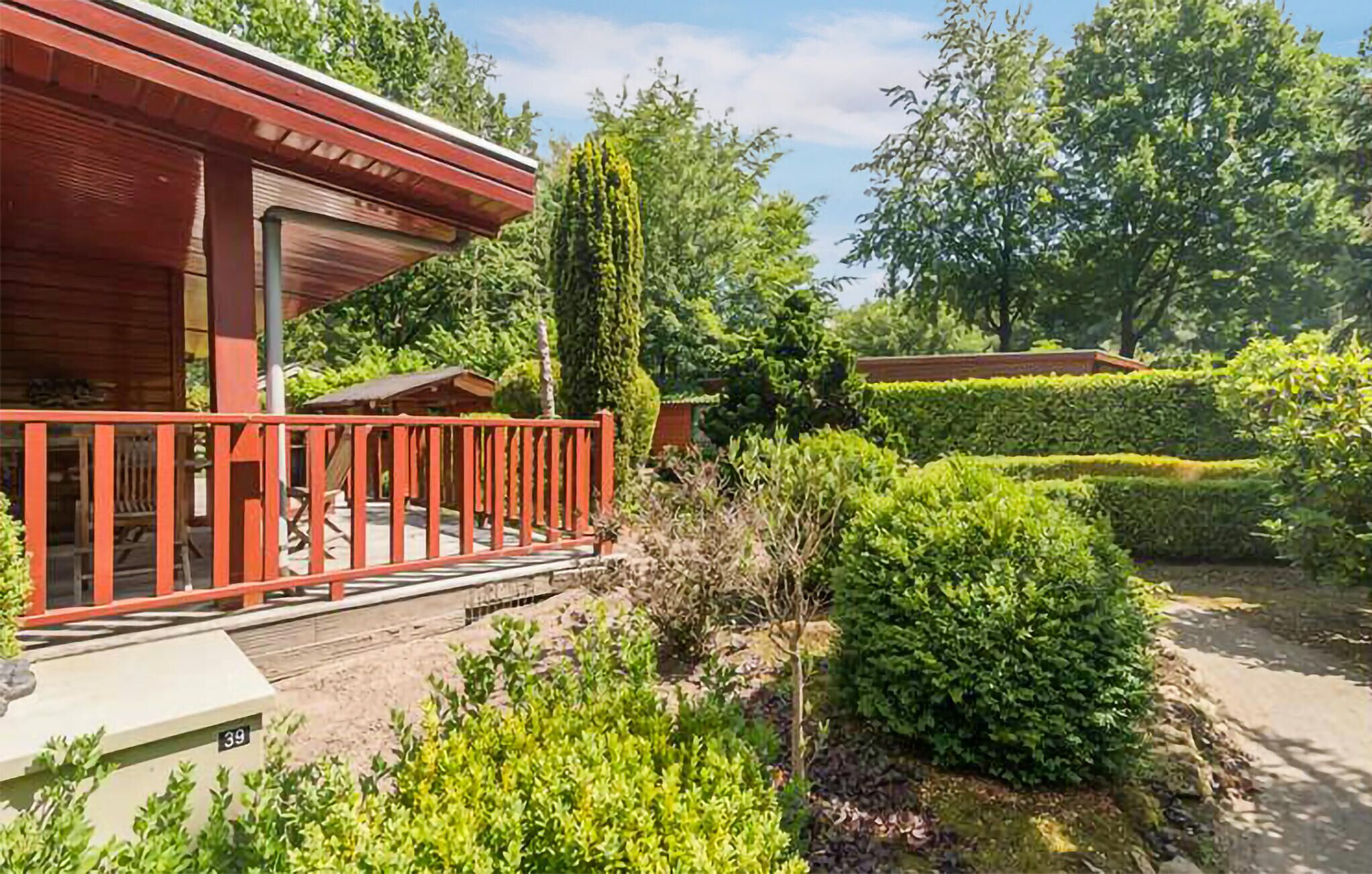 A wooden house with a red balcony, surrounded by well-maintained hedges and trees.