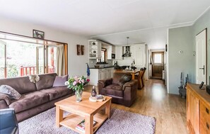 A spacious living area with a sofa, a coffee table, and a dining table. There is a kitchen in the background with cabinets and a window.