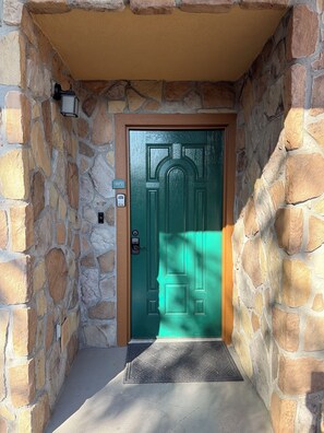 A stone-walled entrance with a green door, a doormat, and a mailbox. - Smoky Bear Crossing - Downtown Corner Condo, Walk to Attractions (Gatlinburg)