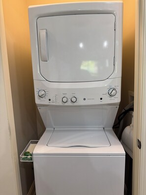 A front-loading washing machine with control knobs, a detergent dispenser, and a white laundry basket. - Smoky Bear Crossing - Downtown Corner Condo, Walk to Attractions (Gatlinburg)