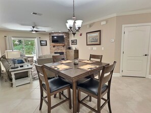 A dining area with a wooden table and chairs, a chandelier, and a television mounted on a stone wall.