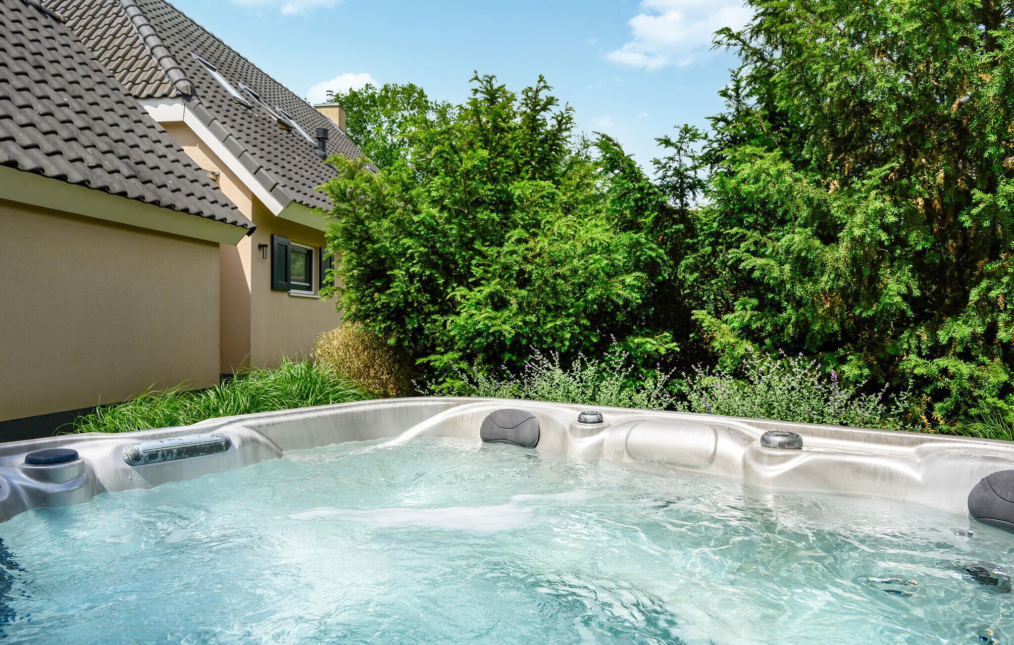 A hot tub in a backyard with a house and lush greenery in the background.