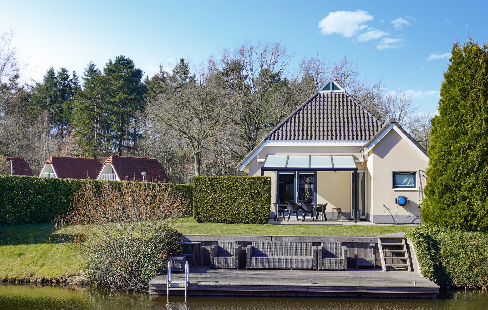 A modern house with a sloped roof, a patio with outdoor furniture, and a dock extending into a body of water.