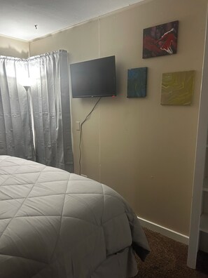 Un dormitorio con una cama, un televisor de pantalla plana montado en la pared y tres cuadros.