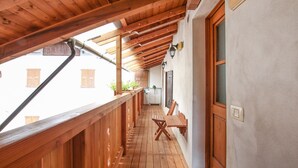 A wooden balcony with a view of a building, a table, chairs, and a door.