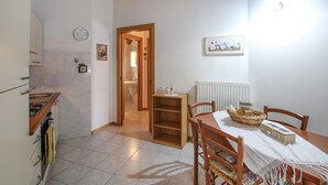 A kitchen with a stove, sink, and cabinets, leading to a bathroom with a toilet and sink. There's a dining table with chairs and a basket of bread.