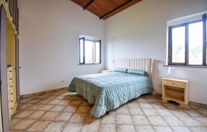 Quarto com cama, janela, mesa de cabeceira e guarda-roupa.