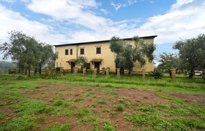 Uma casa de dois andares com telhado de telhas, cercada por um muro de tijolos e árvores.