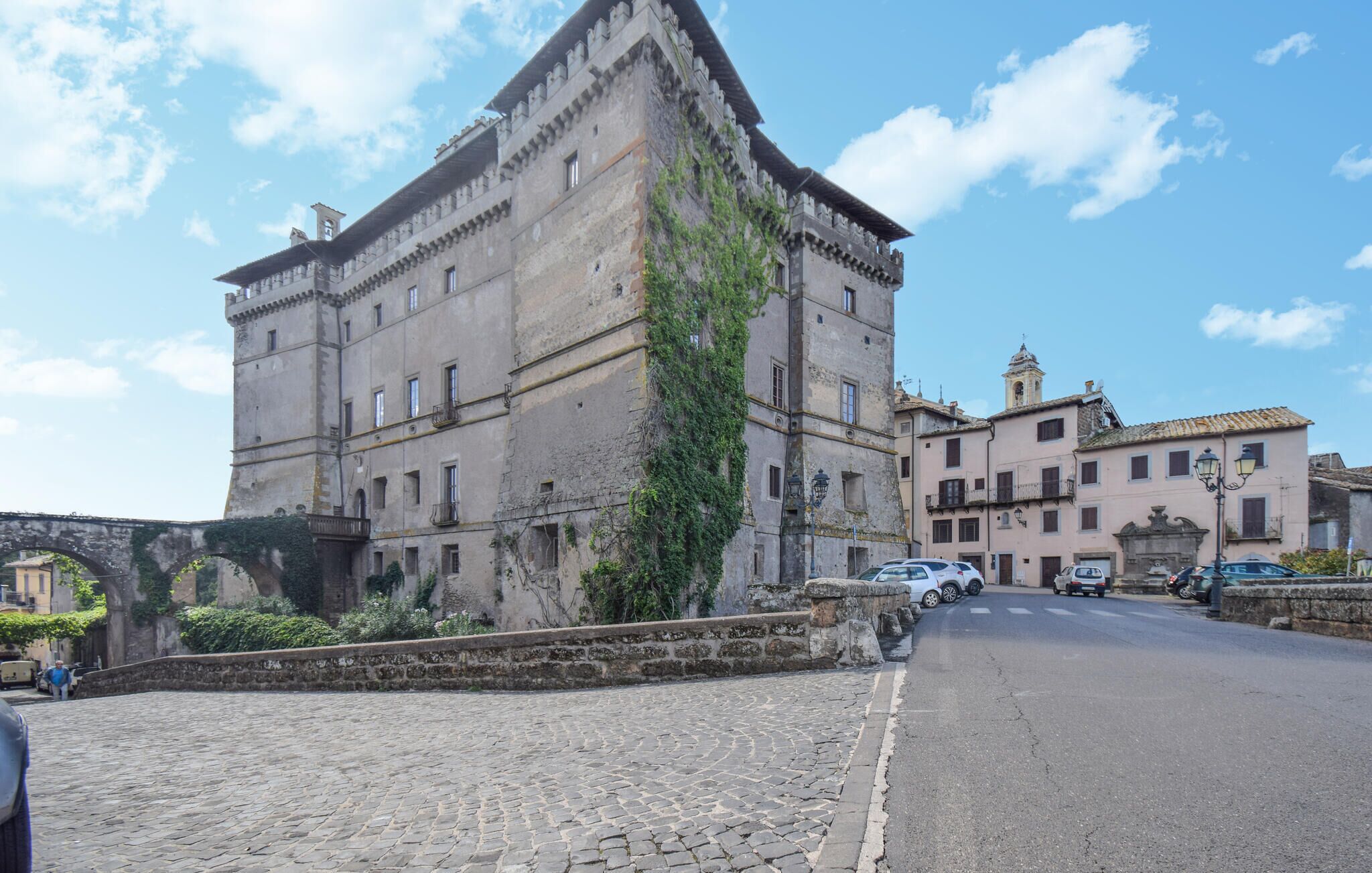 A historic stone building with a tower, a cobblestone street, and a bridge.
