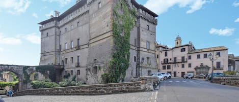 Un edificio histórico de piedra con una torre, una calle adoquinada y un puente.