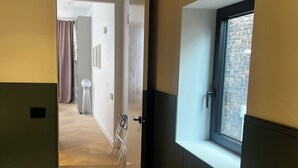 Un couloir doté d’un plancher en bois, d’un tapis blanc et d’une fenêtre donnant sur un mur de briques.