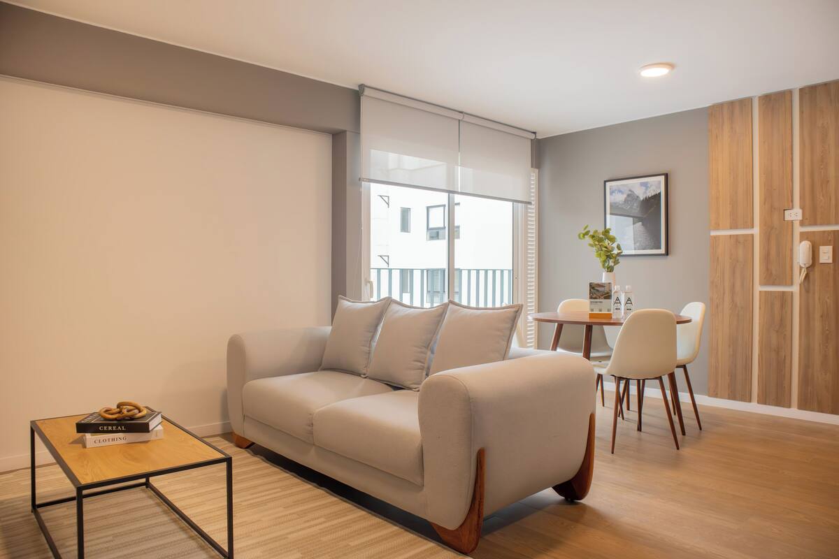 A modern living room with a sofa, a coffee table, and a dining area with chairs and a small table.